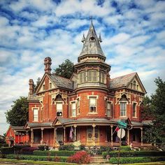 an old red brick house with a turret and steeple on the top, surrounded by greenery