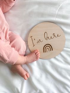 a baby laying on top of a bed holding a wooden sign