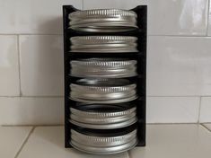 a stack of silver plates sitting on top of a white tile floor next to a wall