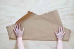 two hands are reaching up towards a piece of brown paper on a wooden table with scissors