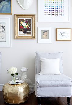 a living room with pictures on the wall and a gold stool in front of it