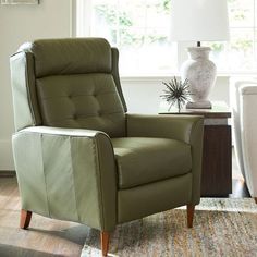 a green recliner chair sitting on top of a rug in front of a window