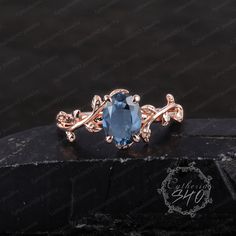 a ring with an oval blue stone in the center and leaves around it on a black surface