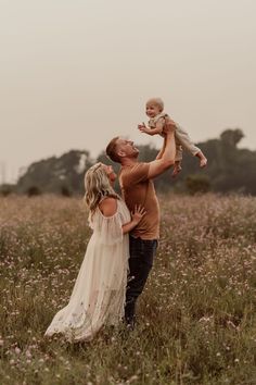 a man and woman holding a baby in a field