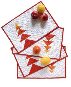 three quilted placemats with apples and oranges on them, one in the shape of an arrow