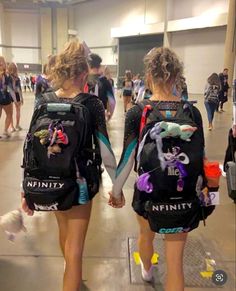 two girls with back packs walking down the hall holding hands and looking at each other