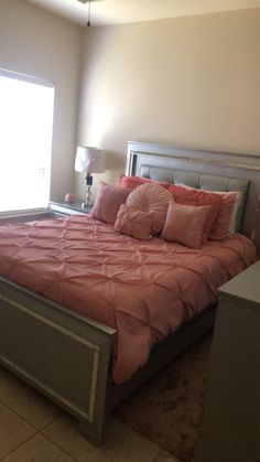 a bed with pink sheets and pillows in a bedroom next to a lamp on a dresser