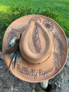 Hand burned sunflower and feather Hillbilly Hippie hat. This beauty is perfect for your next concert, dinner date or any special occasion. It's simply stunning. Hats are one size fits all with a drawstring to adjust sizing. Western Style Top Hat For Summer Festivals, Handmade Country Style Top Hat For Country Events, Western Style Summer Festival Top Hat, Feathered Brimmed Hat Bands For Summer, Brimmed Hat Bands With Feathers For Summer, Adjustable Feather Hats For Country Events, Western Summer Hats With Feathers, Bohemian Feathered Hat Bands For Country Events, Western Summer Hat With Feathers