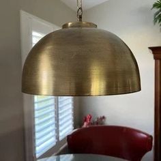 a light hanging over a dining room table with red chairs in front of the window