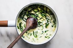 a wooden spoon is in a pot filled with green vegetables and cucumber slices