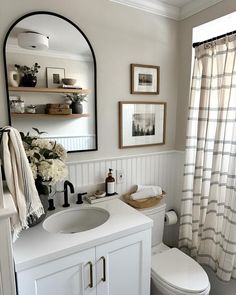 a white toilet sitting next to a sink in a bathroom under a mirror and framed pictures on the wall