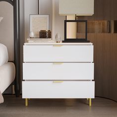 a white dresser sitting next to a bed with a lamp and pictures on top of it