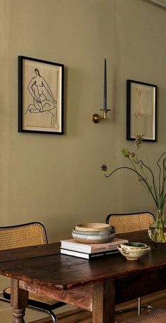 a dining room table with chairs and pictures on the wall above it, along with vases filled with flowers