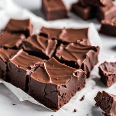 pieces of chocolate cake sitting on top of white parchment paper next to other brownies