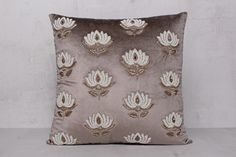 a decorative pillow with gold and silver flowers on it's side, sitting against a white wall