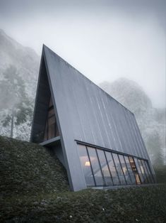 an unusual house on the side of a hill with mountains in the background and foggy sky