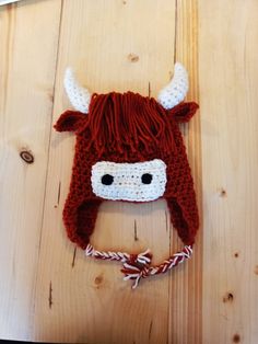 a crocheted hat with a cow's head on it, sitting on a wooden surface