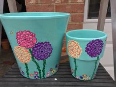 two painted flower pots sitting on top of a metal table next to a brick wall