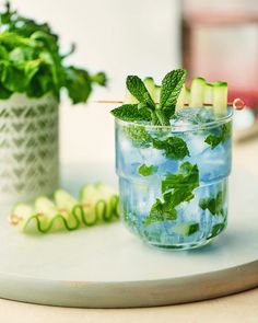 two glasses filled with water and cucumbers on top of a table next to each other