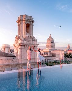 two people standing on the edge of a swimming pool in front of a large building