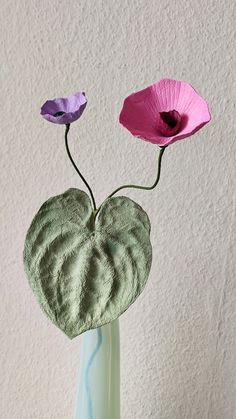 three pink and purple flowers are in a green vase on a table with a white wall behind them