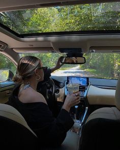 a woman sitting in the driver's seat of a car while holding a drink