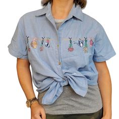 This beautiful chambray blue button-up shirt is perfect for any casual occasion. Made of 100% cotton and featuring delicate flower embroidery, it's both comfortable and stylish. With a chest size of 22.5 inches and a shoulder to hem length of 26.5 inches, it's a great fit for anyone in the M/L size range. The shirt is an original from Basic Editions, made in India in the 1990s. Its style is a mix of secretary and geek, giving it a unique and trendy look. This vintage top is ideal for those who love the cottage core aesthetic and want to add a touch of vintage to their wardrobe. Missing a button near the top Rounded bottom hem Embroidered clotheslined with watering can, gardening gloves, cut flowers , and sunhat Light Blue Cotton Shirt For Spring, Spring Chambray Shirt With Buttons, Light Blue Embroidered Cotton Shirt, Light Blue Cotton Embroidered Shirt, Blue Cotton Shirt With Floral Embroidery, Spring Embroidered Light Wash Tops, Spring Chambray Collared Shirt, Light Wash Embroidered Tops For Spring, Light Indigo Collared Shirt For Spring