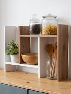 a shelf with bowls, spoons and jars on it next to a potted plant