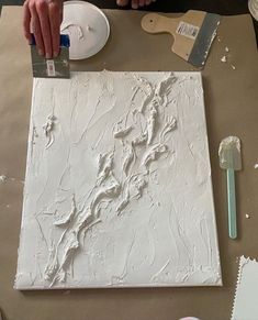 a person is painting on a piece of white paper with paintbrushes and glue