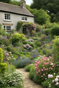 a garden with lots of flowers and plants in front of a white house on a sunny day