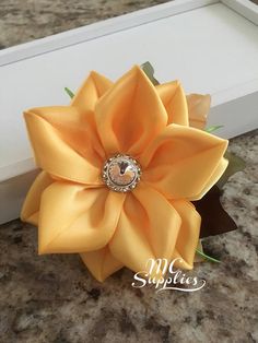 a yellow flower with a diamond center on it's side in a white box