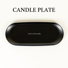 a black candle plate sitting on top of a white table next to the words sand & sea