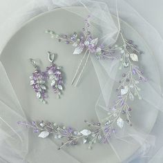 a white plate topped with purple and green flowers next to a pair of silver earrings