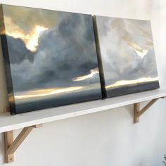 two paintings are sitting on a shelf in a room with white walls and wooden shelves