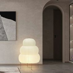 a white lamp sitting on top of a wooden table next to a painting and bookshelf