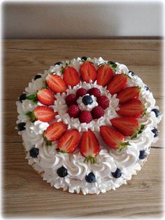 a white cake with strawberries and blueberries on top is sitting on a wooden table