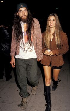 a man with long hair walking next to a woman wearing short shorts and boots on the sidewalk