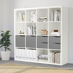 a white bookcase with many books on top of it next to a potted plant