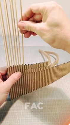 two hands are working on an object made out of cardboard and wood sticks, which is being held by another person's hand