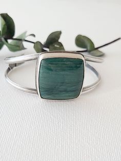 This large square Larsonite* is a deep sea-green color with darker greens sweeping across its surface. Simply set atop a cuff bracelet, the curving lines of silver give this statement cuff an elegant, feminine style. On the underside of the stone, waves of silver are cut away to reveal the beautiful underside of this u Modern Green Cuff Bracelet As Gift, Modern Green Cuff Bracelet Gift, Modern Green Cuff Bracelet For Gift, Handmade Green Cuff Bracelet For Formal Occasions, Modern Green Cuff Bangle Bracelet, Elegant Feminine Style, Sea Green Color, Green Jasper, Elegant Feminine