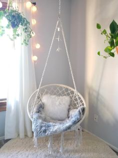 a hanging chair in the corner of a room with white rugs and pillows on it