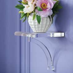 a white vase filled with flowers sitting on top of a shelf next to a blue wall