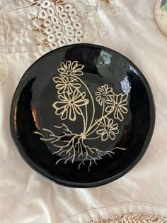 a black plate with white flowers on it sitting on a lace tablecloth and doily