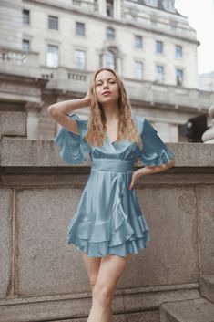 This romantic satin dress will be handmade bespoke for you in London. Cut from luxury fabric, wrinkle-proof, and drapes magnificently along with the silhouette. It features a deep V neck, a side tie fastening,  ruffles, flared skirt, loose sleeves, and a fitted silhouette. This design is super versatile and easy to wear, mixing the quirks of bewitching glam with effortless chic. Perfect for an alfresco lunch with friends, or a romantic city-stroll date. - Dress is partially lined - Mini Length - Elegant Blue V-neck Ruffle Dress, Flowy Ruffle Dress For Wedding, Blue Ruffle Dress For Summer Evening, Summer Wedding Mini Dress With Satin Finish, Elegant Flowy Ruffle Dress For Wedding, Blue Ruffled Mini Dress For Wedding, Satin Tiered Dress With Ruffles, Tiered Satin Dress With Ruffles, Blue V-neck Dress With Satin Finish