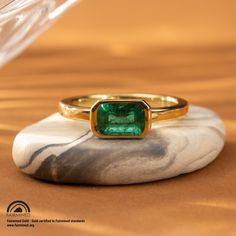 Expertly crafted with a vivid 1.36 carat Zambian emerald set horizontally, the Latitude Emerald Ring exudes elegance. Made with Fairmined yellow gold, this vibrant ring is both luxurious and socially responsible. Own a piece of beautiful jewelry while supporting ethical mining practices. Design Specifications: Type: Ring Material: 18 karat Fairmined yellow gold Width: 2.4mm Thickness: 2mm Finish: Polished Profile: Flat with rounded edges Setting Style: East/West Bezel Stone Specifications: Type: Modern Yellow Gold Emerald Ring For May Birthstone, Classic Gold Ring With Tsavorite, Fine Jewelry Emerald Ring With Tension Setting, Modern Yellow Gold Emerald Ring, Yellow Gold Emerald Ring With Tension Setting As Gift, Modern Gia Certified Emerald Ring Gift, Yellow Gold Emerald Ring With Tension Setting, Classic Yellow Gold Emerald Ring With Tension Setting, Radiant Cut Emerald Ring In Yellow Gold