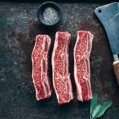 raw steaks on a cutting board next to a knife and peppercorin sprig