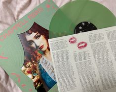 a green vinyl record sitting on top of a bed next to a book and magazine