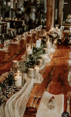 a long wooden table with candles and flowers on it, along with other place settings