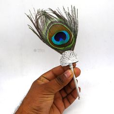 a hand holding a small metal object with a peacock feather on it's tip