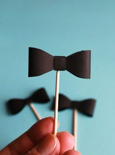 a hand holding two brown bow tie lollipops